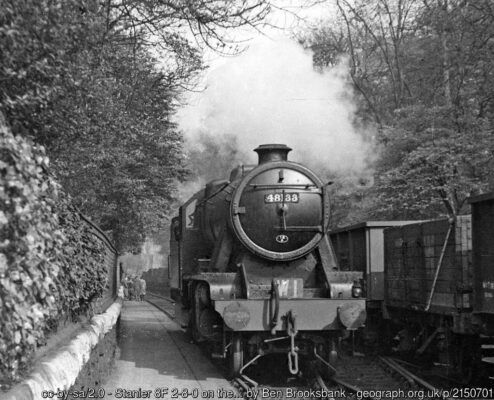 Believe it or not, this IS in Crewe Works. The 2-8-0, No 48133 (built 1941, withdrawn 11/66) is on Works Pilot job W1, is running on the 'Deviation Line' (originally the main Crewe - Chester line before the great expansion of the Works in July 1878. The view is eastward, between Flag Lane and Chester bridges. The occasion was a visit by the Railway Correspondence & Travel Society; some of my companions can be glimpsed ahead, outside the entrance to the General Offices